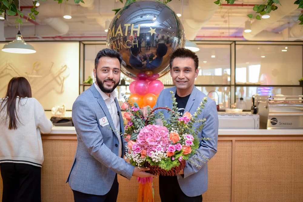 Two Bidmath team members with flowers and balloons at the launch event